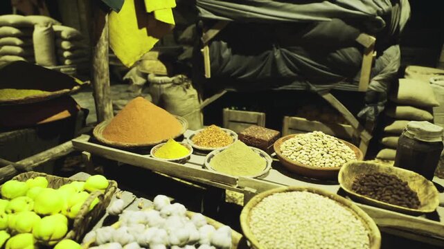 Evening bazaar stalls with spices and fruit, melange of sacks, bowls and crates under warm lamps, leafy green produce contrasts with amber spice mounds, lively