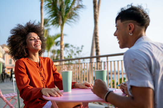 Beautiful woman with curly hair enjoying a cold drink at a trendy pink table in a coastal town