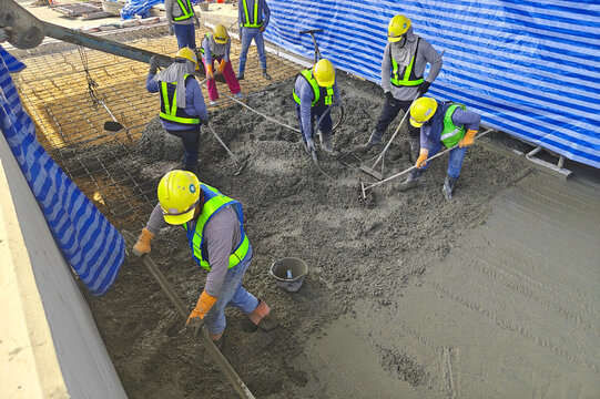 Workers pouring and leveling concrete wearing safety gear.
