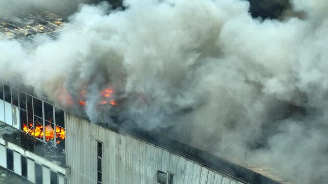 Drone shot of a factory engulfed in flames and smoke, symbolizing extreme events, climate impact, pollution, and the global transition toward sustainability and net zero goals. 4k.

