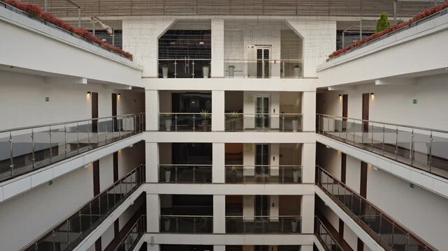 Open atrium modern office lobby multilevel balconies with glass railings, central wooden deck planters with greenery, daylight