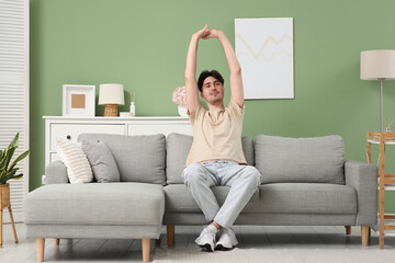 Obraz premium Young man stretching on grey sofa at home