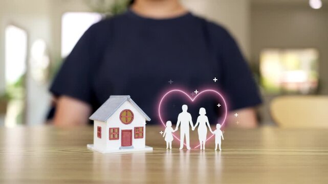 Family life insurance and home protection concept with small house model and paper family silhouette under glowing heart on wooden table