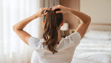 Fototapeta premium Woman Arrange Hair into Ponytail in Bedroom, Close-up View from Back