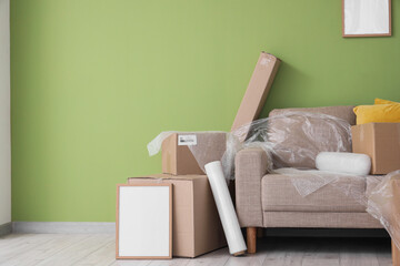 Sofa with film and cardboard boxes near green wall in room on moving day © Pixel-Shot