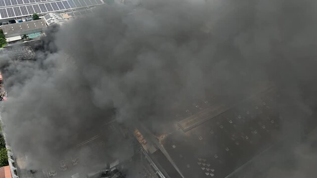High-angle aerial shot of a factory engulfed in smoke, spreading emissions into the atmosphere, highlighting environmental hazards, industrial risks, and air pollution concerns. 4k.
