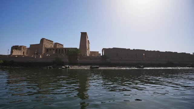 Scenic view of the Philae Temple on the Nile River, surrounded by water and rocky landscape, highlighting ancient Egyptian architecture and tranquil atmosphere.