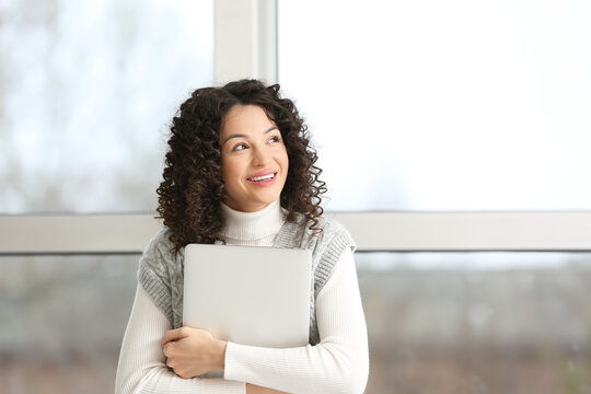 Young businesswoman with laptop looking upwards near window in office
