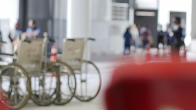 Row of hospital wheelchairs parked outside medical facility entrance with security guard in healthcare service