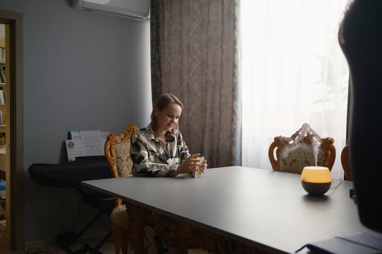 Woman reading tarot cards at a dining table with aromatic diffuser and ornate chairs