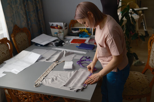 Home dressmaker measuring and cutting fabric in a small sewing workshop at a dining table