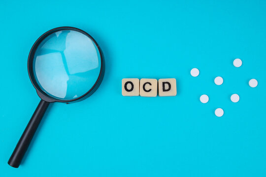 Top View Of Magnifying Glass Near OCD Word Tiles And Scattered Pills For Mental Health Concept