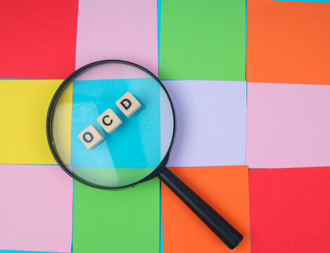 Top View Of Magnifying Glass Over OCD Tiles On Colorful Grid For Mental Health Concept