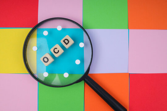 Magnifying Glass Over Skewed OCD Tiles And Pills On Colorful Grid For Mental Health Concept