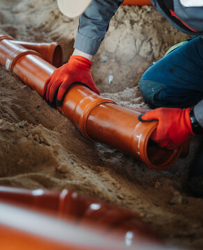 Close-up of worker joining PVC sewer pipes in sand trench. Underground drainage installation with focus on pipe connection and alignment.