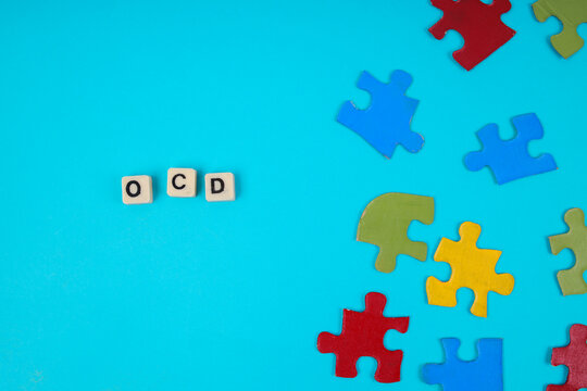 Top View Of OCD Letter Tiles Next To Scattered Puzzle Pieces On Blue Background For Mental Health Concept