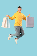 Handsome young man with shopping bags jumping on blue background