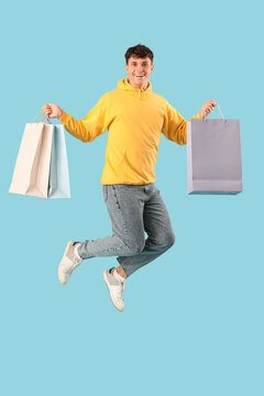 Handsome young man with shopping bags jumping on blue background