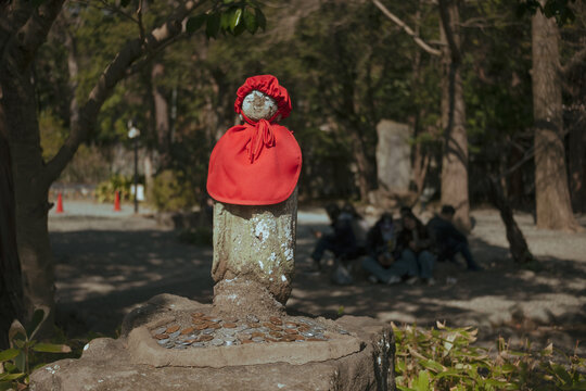 Traditional Japanese Jizo stone statue with red bib and hat in a forest temple