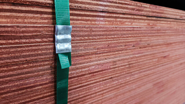 Close up of stacked plywood sheets secured with plastic strap, wood panel texture background for construction, carpentry, warehouse and industrial material concept.