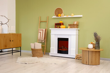 Naklejka premium Interior of stylish room with table, vintage radio receiver and pumpkins on modern fireplace near green wall