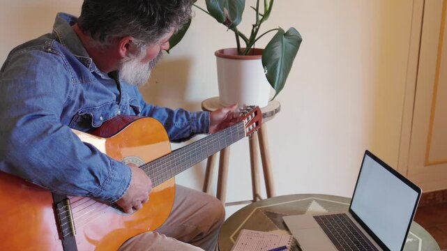 Man with beard tuning acoustic guitar at home
