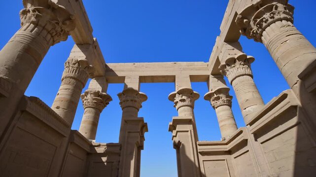 Stunning worm's eye view of Ptolemaic column capitals and architrave at Philae temple of Isis, Aswan, Egypt, framing deep blue Egyptian sky between ancient stones.