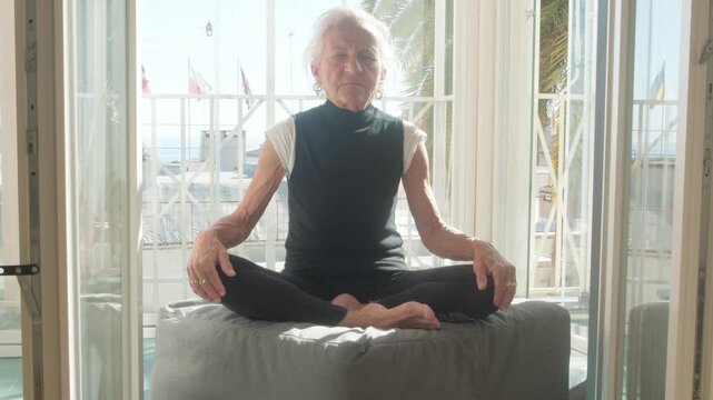 Serene shot of a senior woman practicing yoga and meditation in a lotus pose at home. Focus on healthy aging, mental clarity, and physical wellness for the elderly