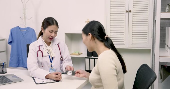 Obstetrician holding ultrasound image while explaining to Asian pregnant woman during prenatal consultation showing medical care and positive relationship during third trimester maternity checkup