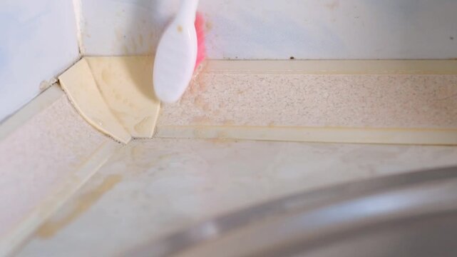 Gloved hand wiping grout seam with cloth after brushing, final polishing and drying of tile edge by sink, closeup showing removal of foam and residual dirt, neat domestic finishing