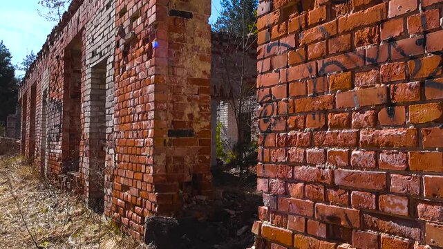 Ruined and crumbling red brick building without a roof, slowly being reclaimed by nature in a forgotten forest with debris and rubble scattered around the deteriorating structure