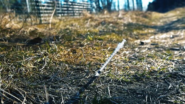 Dangerous used syringe discarded in a public park, a symbol of drug addiction, abuse, and health risks from hypodermic needles left in the environment, with a blurred background