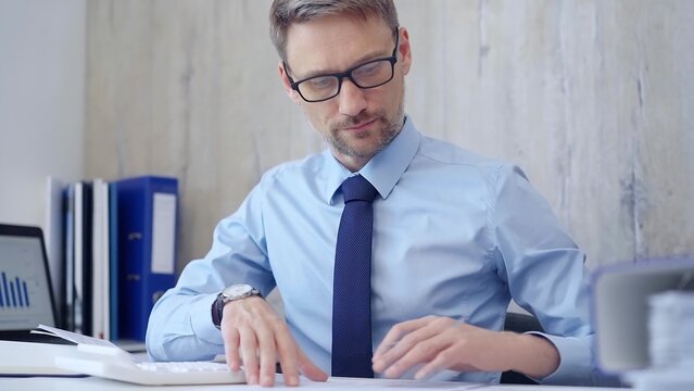 Male accountant with blue t-shirt concentrating while calculating costs and taking notes at his desk. Taxes, audit in business