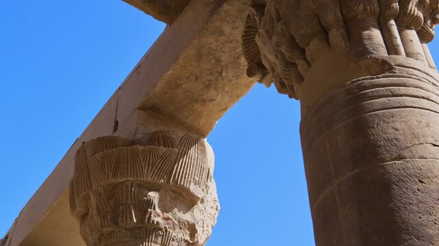 Stunning worm's eye view of Ptolemaic column capitals and architrave at Philae temple of Isis, Aswan, Egypt, framing deep blue Egyptian sky between ancient stones.