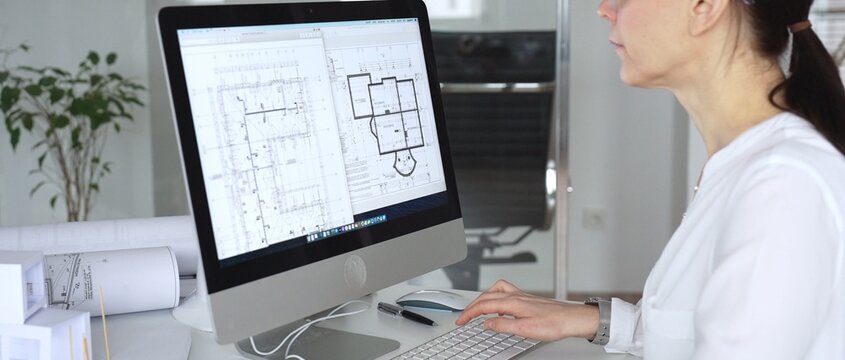Architect woman working on blueprints and building plans using computer aided design in modern office. Business and architecture concept