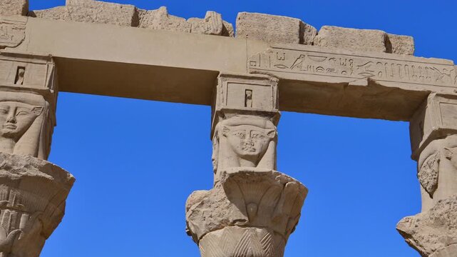 Row of ancient Egyptian columns topped with carved Hathor faces and papyrus floral capitals inside Philae temple complex, Agilkia Island, Aswan, Egypt.
