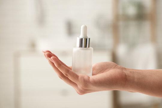 Female hand holding bottle of cosmetic product in bathroom, closeup
