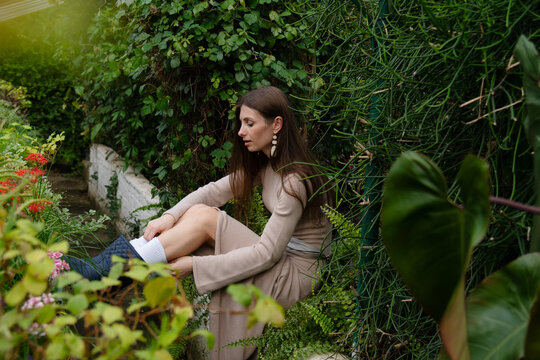 Girl sitting among plants while in a garden or greenhouse in the daytime