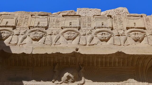 Iconic Hathor-headed columns with carved goddess faces and papyrus capitals at Philae temple, Aswan, Egypt, supporting hieroglyphic architrave against vivid deep blue sky.