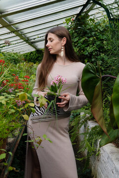Woman holding a flower pot while standing among plants in a greenhouse during daylight hours