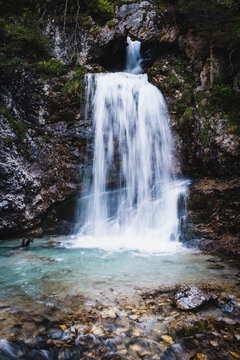 Cascate di Vallesinella waterfall through rock arch into turquoise pool, long exposure silky water, Madonna di Campiglio Trentino Italy