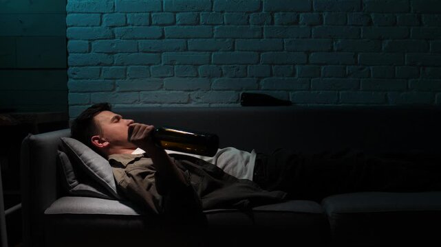 Man lying unconscious on a sofa, holding an empty alcohol bottle, highlighting themes of drinking, addiction, loneliness, and depression in a dimly lit room