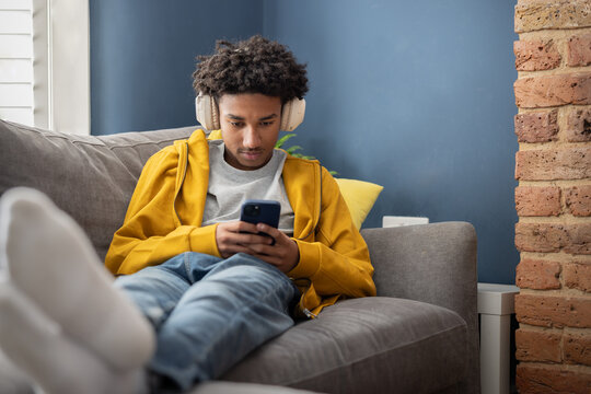 Teen boy in Headphones Using Smartphone on Couch