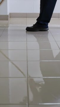 Vertical video: Mopping worker in dark pants pushing blue mop contacting tile, cleaning hall floor