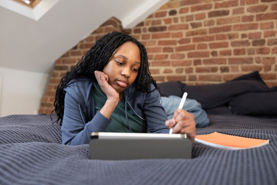 Teen girl thoughtfully studying on her tablet in bed
