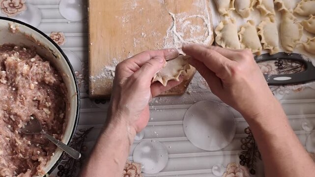 Hands forming dumplings with meat filling on kitchen table, traditional homemade food.