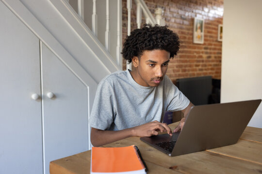 Focused teenage boy engaged with a laptop doing his school work