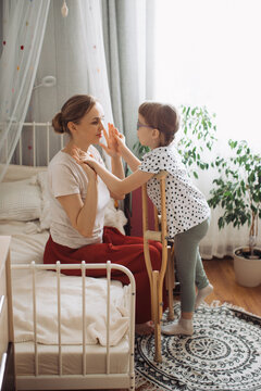 Mother and child bonding indoors, girl using crutches