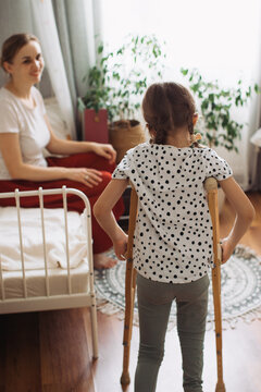 Girl with crutches standing while mother watching