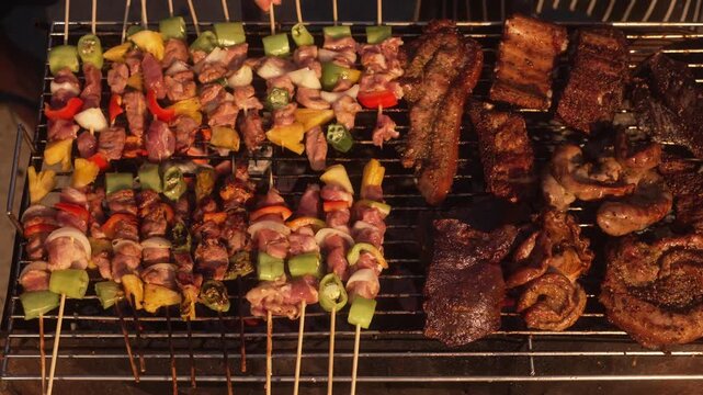 Assorted meats and vegetable kebabs grilling on a barbecue, with ribs and steaks searing on metal grate, warm smoky outdoor cookout food scene.